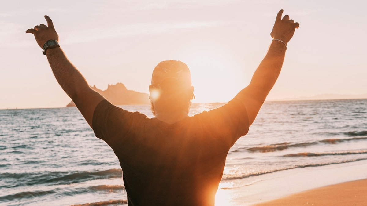man in black shirt raising his hands on beach during daytime